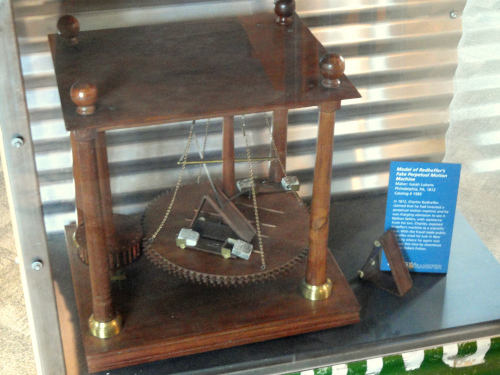 perpetual motion machine - wood frame with four posts, small wooden gear to left and large wooden gear in center