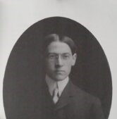 A sepia-toned oval portrait of a young man, Charles Harper Smith, circa 1900. He is wearing wire-rimmed glasses, a dark three-piece suit, a white collared shirt, and a tie. His name is printed in elegant white cursive and serif typography at the bottom against a black background.