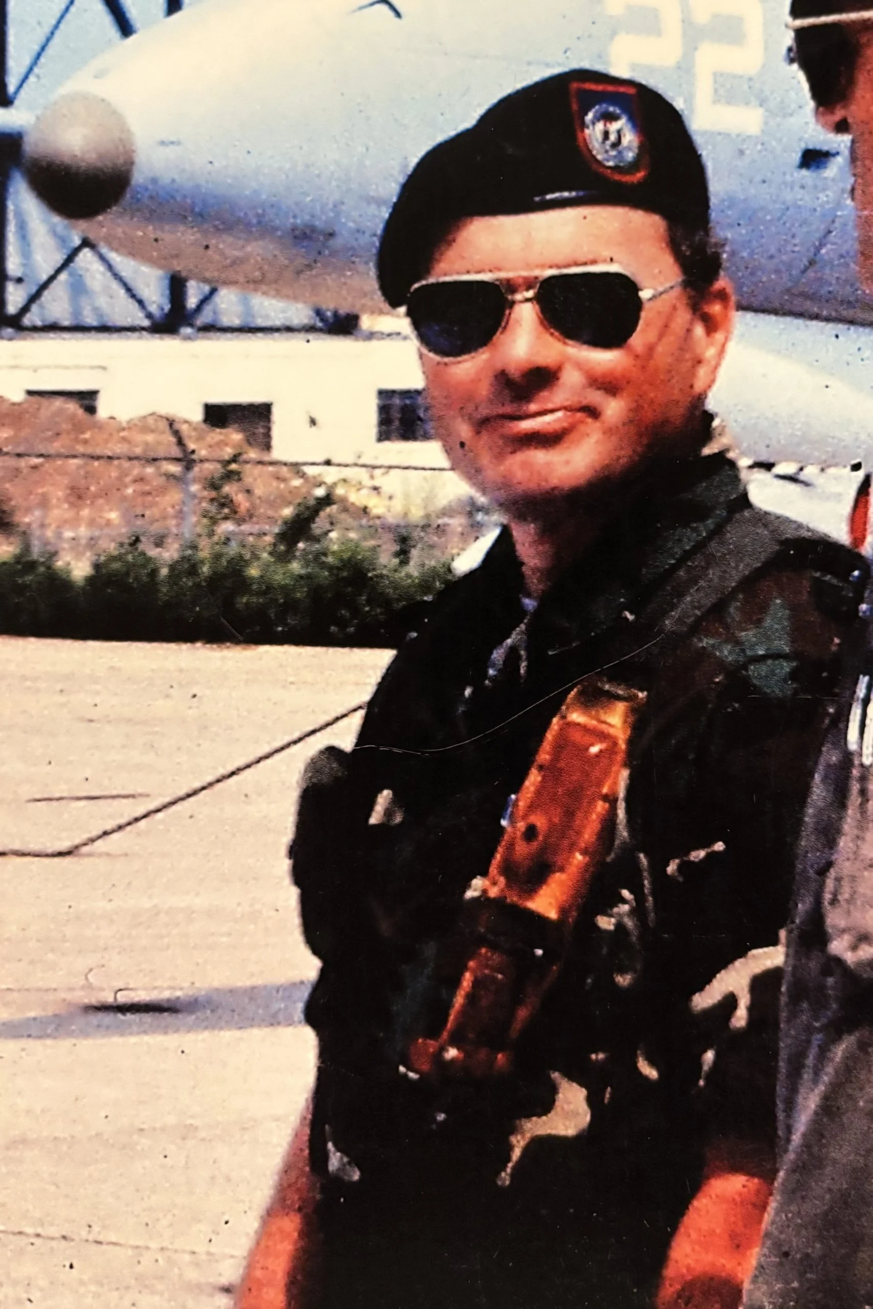 photo of larry glemser in camouflage uniform, black beret, and sunglasses standing in front of an aircraft. 