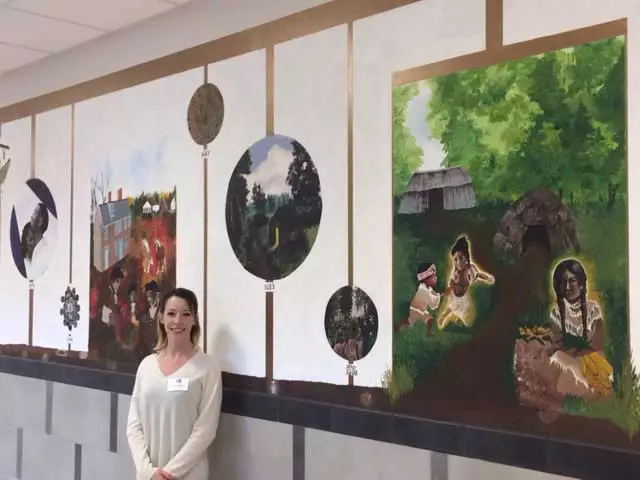 photo of artist Justine Musick in front of historical mural at hallowell elementary school