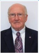 A formal portrait of Wayne Watson wearing a suit and a purple patterned tie.