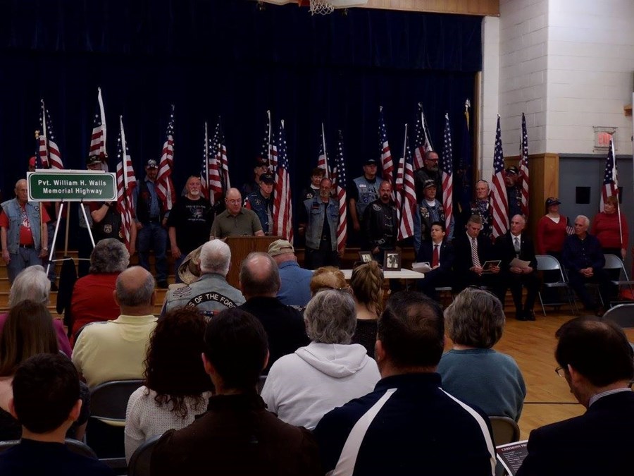 Interior photo of the official designation ceremony for the Pvt. William H. Walls Memorial Highway, showing the unmonitored highway sign and many attending veterans on stage.